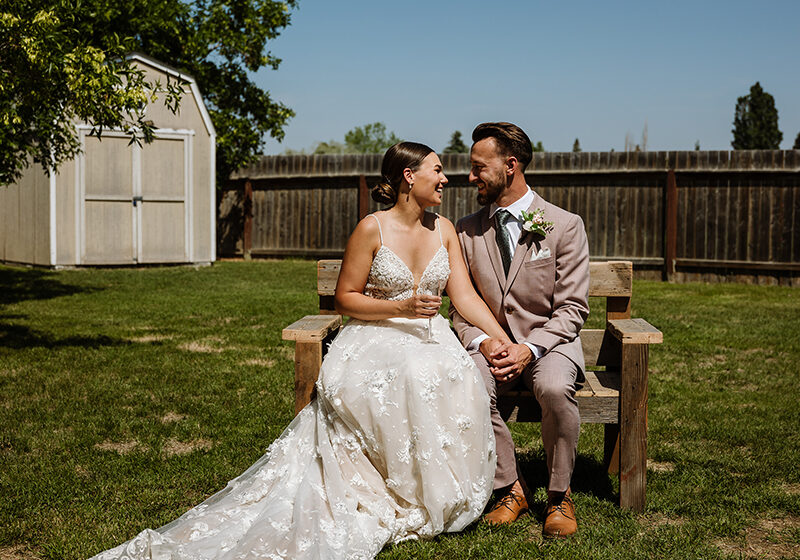 Bride and groom sit on a gifted handmade bench at their backyard wedding in Saskatoon.