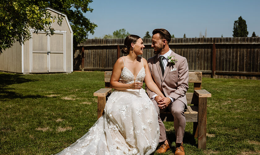 Bride and groom sit on a gifted handmade bench at their backyard wedding in Saskatoon.