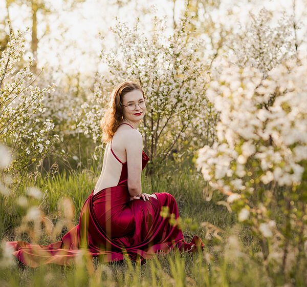 High school grad wears a stunning deep red gown for her cherry blossom graduation photos in Saskatoon.