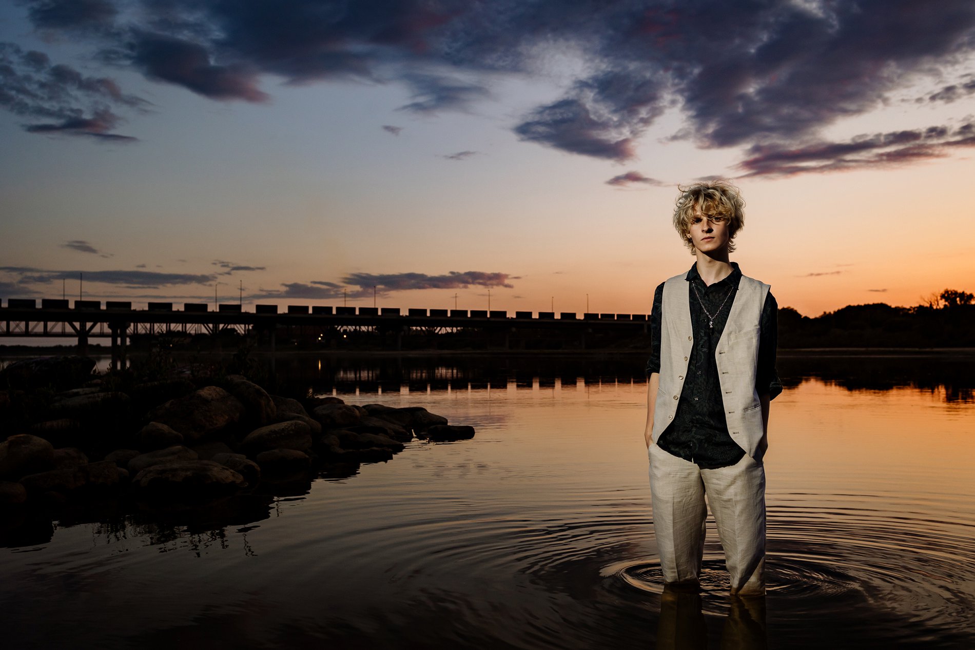 Saskatoon grad photography. A boy stands in the South Saskatchewan River at sunset as a train passes on the bridge in the background.