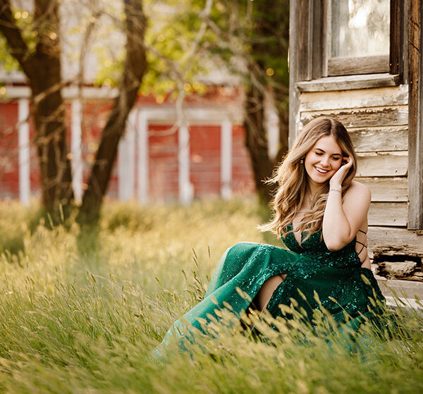 A grad in a sparkly emerald green dress poses at a farm for her LCBI graduation photos near Outlook, Saskatchewan.