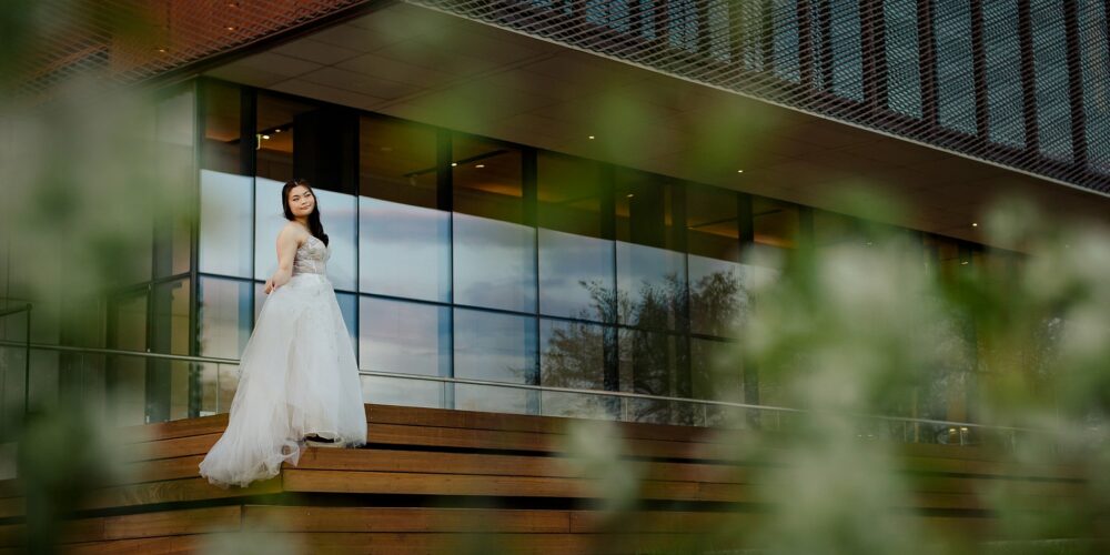 High school graduate in flowing dress on the steps of the Remai Modern at sunset.
