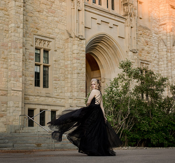 Saskatoon high school girl in long black grad dress dances in front of a building on the University of Saskatchewan campus .